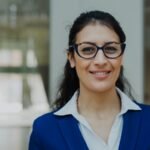 A smiling woman wearing glasses and a blue suit.